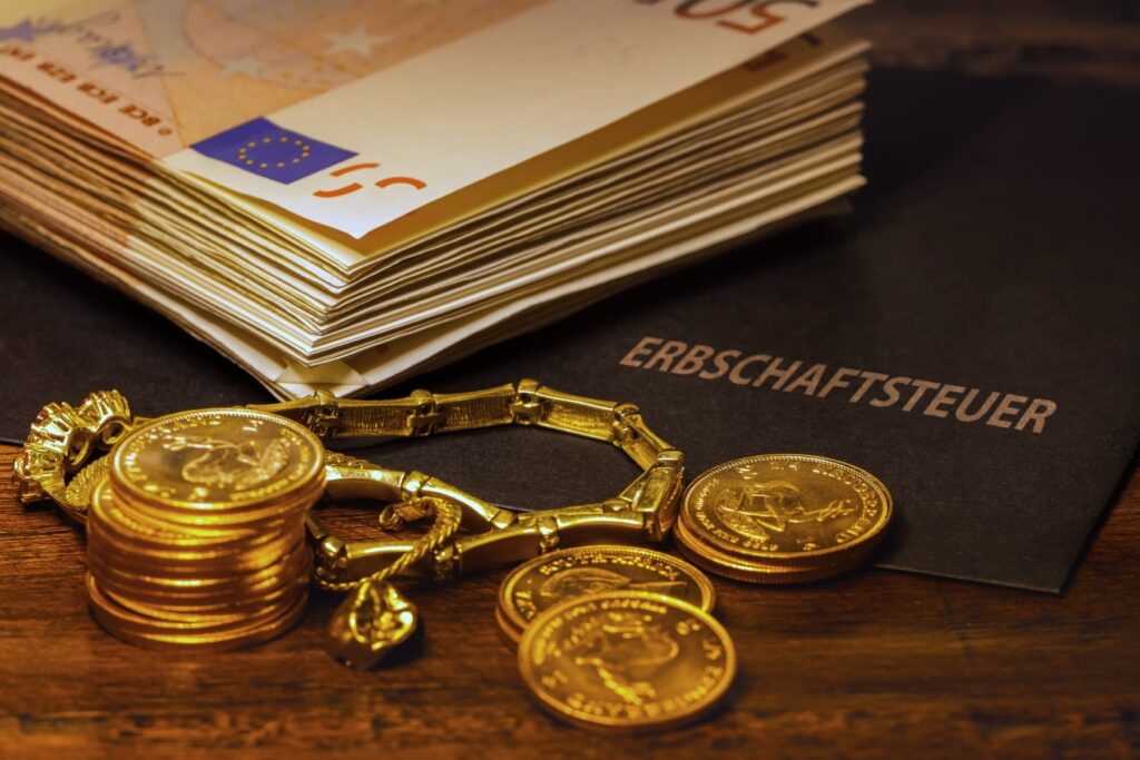 Bargeld, Goldmünzen und Schmuck symbolisieren steuerpflichtiges Erbe neben einem Dokument mit dem Titel „Erbschaftsteuer“ – Beratung durch Steuerberater Gojowsky in Erlangen.